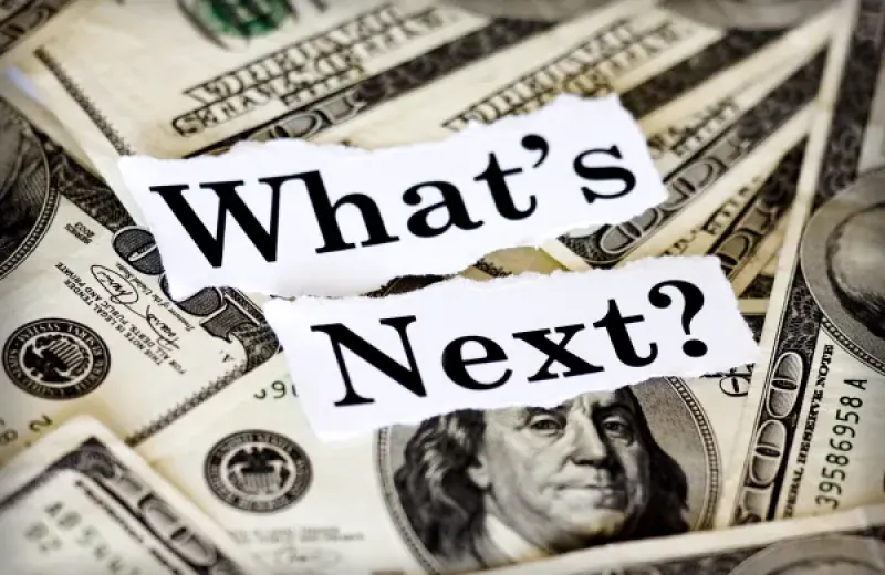 Stacks of dollar bills with a sign reading "What's Next?" on top